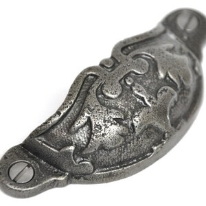May include: A silver-toned metal drawer pull with a decorative floral design. The pull is shaped like a half-circle and has a screw on each end.