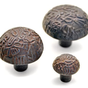 May include: Three antique-style cabinet knobs with a rustic brown finish. Each knob features a unique, intricate design of swirling patterns.