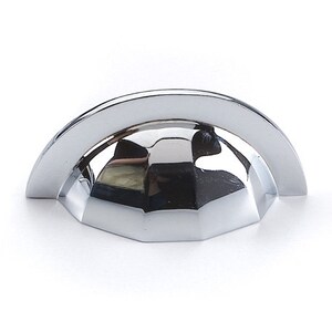 May include: A polished chrome cabinet pull, featuring a half-moon design. The pull has a curved top and a faceted base. The reflective surface creates highlights and shadows. This hardware is suitable for drawers and cabinets. The measurements are in centimetres.
