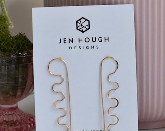 May include: Gold earrings with a wavy design. The earrings are displayed on a white card with the text "Jen Hough Designs" and a website address.