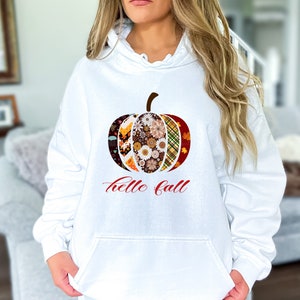 May include: White hooded sweatshirt with a colorful patchwork pumpkin design and the text "hello fall" in red.