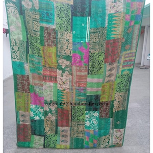 May include: A patchwork quilt made from colorful fabric scraps. The quilt is primarily green with accents of pink, red, and yellow. The quilt is hand-stitched and has a rustic, vintage look.