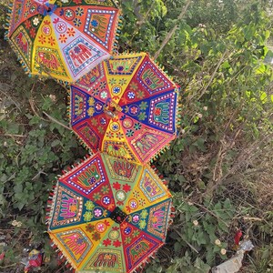 Op de afbeelding: Drie kleurrijke parasols met ingewikkelde borduursels en spiegelversieringen. De parasols zijn gemaakt van stof en hebben een traditioneel Indiaas ontwerp.
