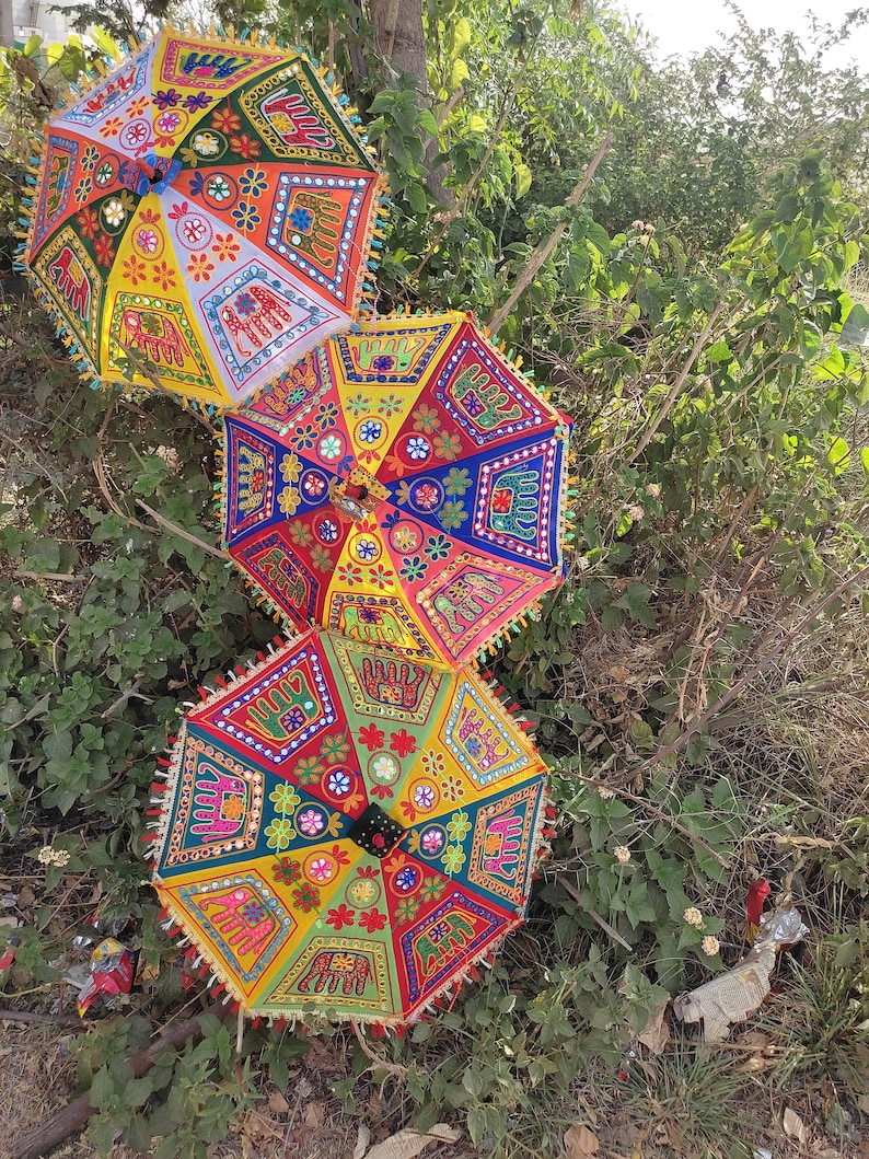 Op de afbeelding: Drie kleurrijke parasols met ingewikkelde borduursels en spiegelversieringen. De parasols zijn gemaakt van stof en hebben een traditioneel Indiaas ontwerp.