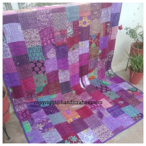 Könnte beinhalten: Ein Patchwork-Quilt in Lila-, Magenta- und Violetttönen. Der Quilt besteht aus verschiedenen Stoffquadraten mit unterschiedlichen Mustern und Texturen, die mit weißem Faden zusammengenäht sind. Der Text "copyright@handicraftexports" ist sichtbar.