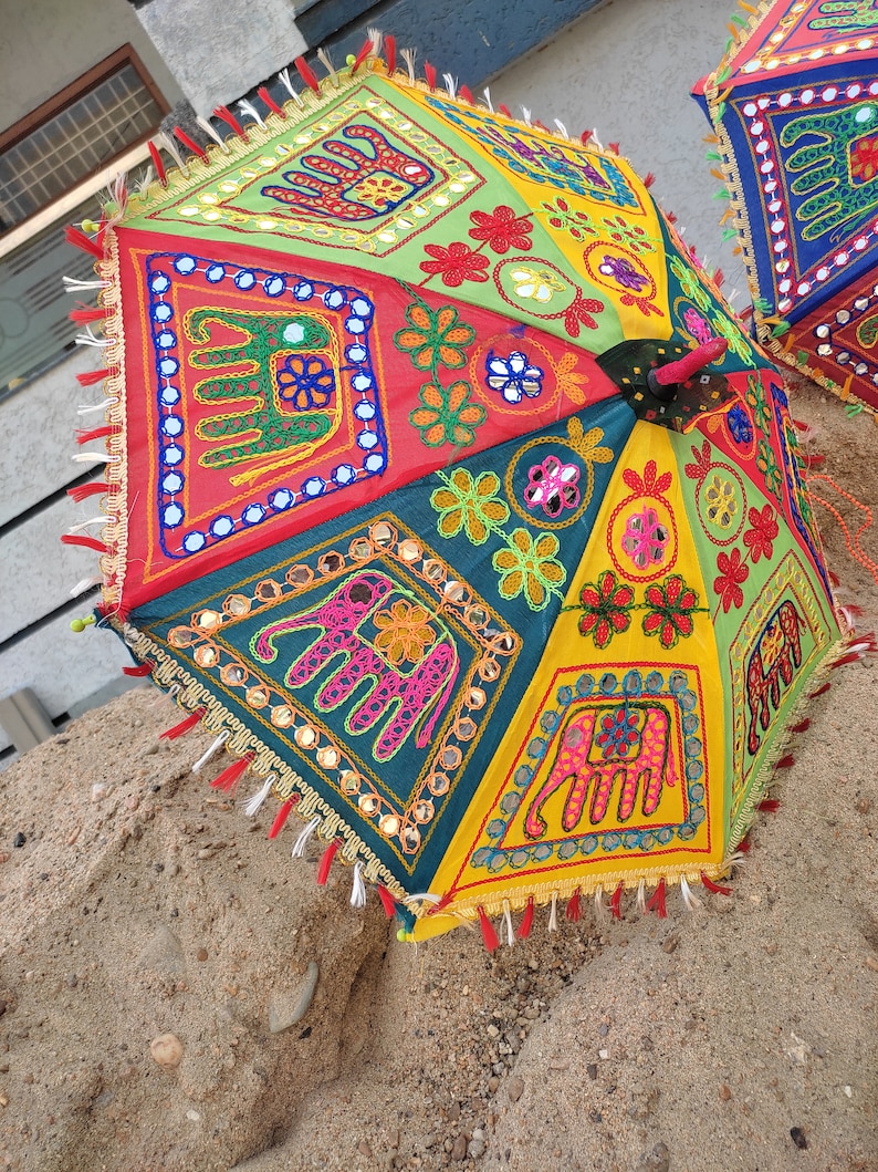 May include: A colourful, multi-panel umbrella with embroidered elephants and floral designs. The umbrella is made of fabric and has a fringe trim.