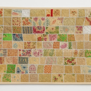 May include: A framed patchwork textile art piece. The artwork is composed of numerous fabric squares in various colors and patterns, including floral and geometric designs. The frame is a light wood color.
