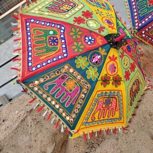May include: A colorful, multi-panel umbrella with embroidered elephants and floral designs. The umbrella is made of fabric and has a fringe trim.