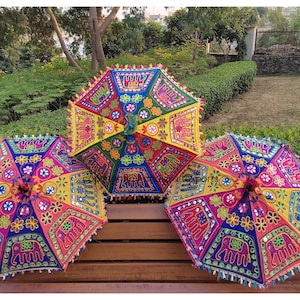 May include: Three colourful umbrellas with embroidered elephant designs and mirror accents. The umbrellas are made of fabric and have a traditional Indian style.