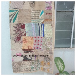 May include: A patchwork quilt made from various fabrics in shades of brown, beige, red, blue, and green. The quilt is made up of squares of different sizes and patterns, and is hand-stitched. The quilt is hanging on a wall, and the text "copyright@handicraftexports" is visible in the lower right corner.