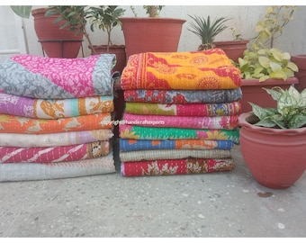 May include: A stack of colorful kantha quilts, also known as kantha blankets, made from recycled saris. The quilts are layered in a variety of colors and patterns, including pink, orange, yellow, blue, green, and white. The quilts are arranged in two stacks, with each stack containing approximately 10 quilts.