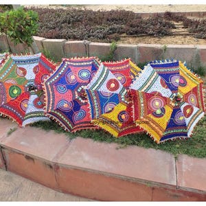 Op de afbeelding: Een set van zes kleurrijke, gepatroneerde parasols met franjes. De parasols zijn gemaakt van stof en hebben een verscheidenheid aan kleuren en ontwerpen, waaronder rood, blauw, geel, groen en wit.