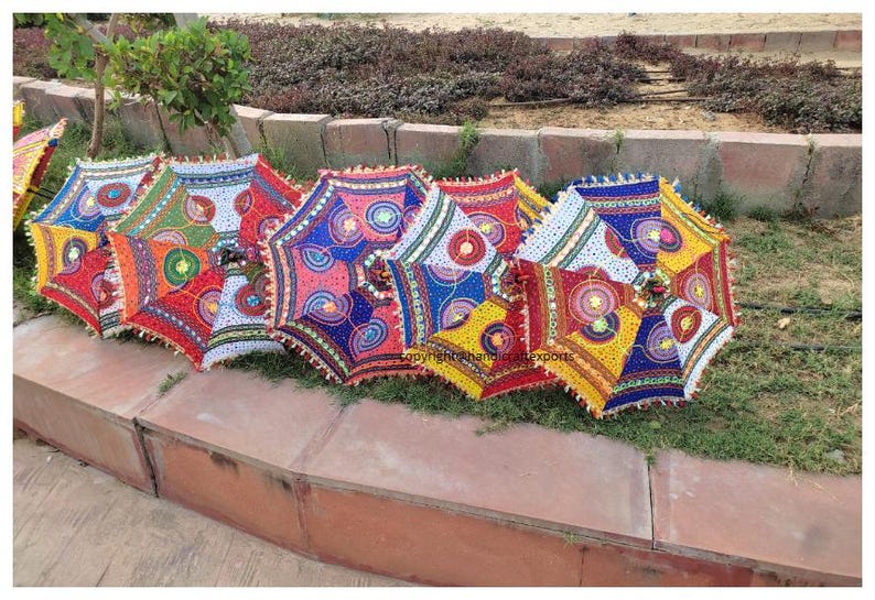 Op de afbeelding: Een set van zes kleurrijke, gepatroneerde parasols met franjes. De parasols zijn gemaakt van stof en hebben een verscheidenheid aan kleuren en ontwerpen, waaronder rood, blauw, geel, groen en wit.