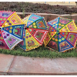 May include: Three colourful umbrellas with embroidered designs, including elephants, flowers, and geometric patterns. The umbrellas are made of fabric and have a fringe trim.