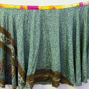 May include: A green wrap skirt with a floral pattern and colorful trim. The skirt is made of recycled saris and has a unique, bohemian style.