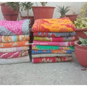 Può includere: Una pila di trapunte kantha colorate, anche conosciute come coperte kantha, realizzate con sari riciclati. Le trapunte sono sovrapposte in una varietà di colori e motivi, tra cui rosa, arancione, giallo, blu, verde e bianco. Le trapunte sono disposte in due pile, ogni pila contiene circa 10 trapunte.