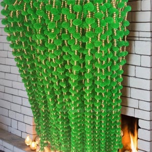 Puede incluir: Guirnalda verde y dorada hecha de pompones y cuentas. La guirnalda está colgada en una pared de ladrillo con una chimenea en el fondo.