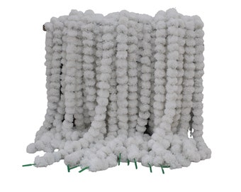 May include: White artificial flower garland made of pom poms. The garland is hanging in a vertical line and is made of many small white pom poms.