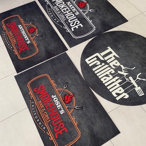 Pu&ograve; includere: Una collezione di tappeti neri rettangolari e circolari con loghi di ristoranti. I tappeti presentano i nomi "Nate's Smokehouse", "Anthony's Smokehouse", "Jose's Smokehouse" e "The Grillfather" in testo bianco e rosso.