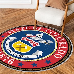 Könnte beinhalten: Runder Teppich mit einem rot-weiß-blauen Design, das das Staatssiegel von Colorado zeigt. Das Siegel zeigt einen goldenen Schild mit einer Spitzhacke und einem Hammer, umgeben von einem blauen Kreis mit den Worten "State of Colorado" und "Nil Sine Numine" in Weiß. Das Siegel ist umgeben von einem roten Ring mit weißen Sternen und dem Jahr "1876" in Weiß.