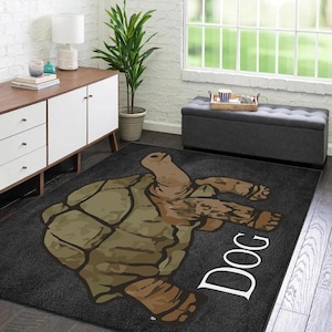 May include: A black and gray area rug with a cartoon turtle design and the word "Dog" in white text. The rug is on a hardwood floor with a white wall and a plant in the background.