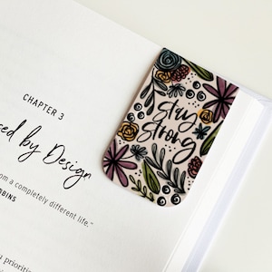 May include: A floral bookmark with the text "Stay Strong" in black script. The bookmark has a pink background with colorful flowers and leaves.