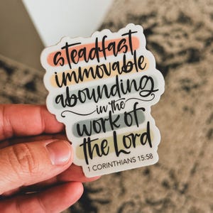 May include: A white sticker with colorful stripes and black text that reads "steadfast immovable abounding in the work of the Lord 1 Corinthians 15:58".