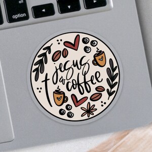 May include: A round sticker with the text "Jesus & Coffee" in a handwritten style. The design includes coffee beans, coffee cups, hearts, and floral elements in brown, black, and cream colors. The sticker is on a laptop.