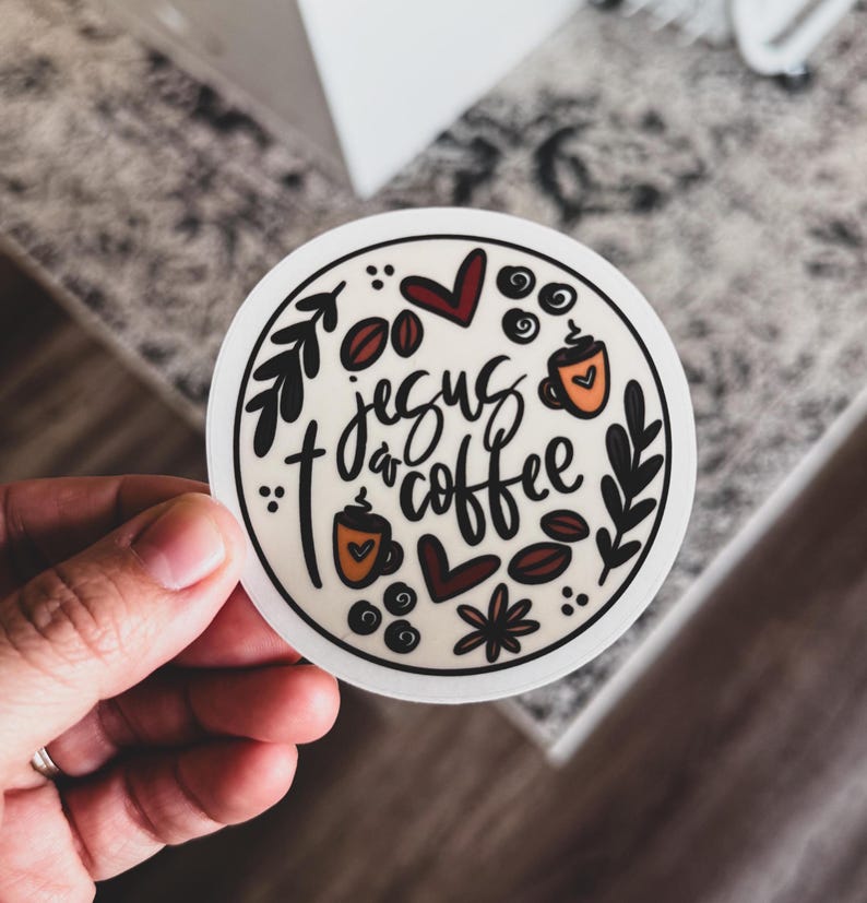 May include: A round sticker with the words "Jesus & Coffee" in black script. The sticker features coffee beans, hearts, and coffee cups in brown, orange, and black, with a white border.