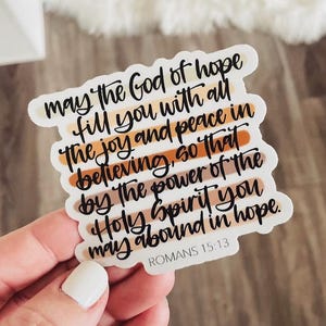 May include: A sticker with a colorful striped background and the text "may the God of hope fill you with all the joy and peace in believing, so that by the power of the Holy Spirit you may abound in hope. ROMANS 15:13"