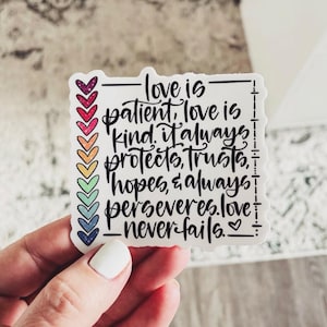 May include: A white sticker with a rainbow of hearts on the left side and a black and white quote on the right side. The quote reads "Love is patient, love is kind. It always protects, trusts, hopes, & always perseveres. Love never fails."