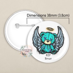 May include: A round button badge featuring a teal teddy bear with angel wings and a halo. The text "RIP Bruv" is below the bear. The badge is 38mm in diameter. The badge has a white backing and a metal pin.