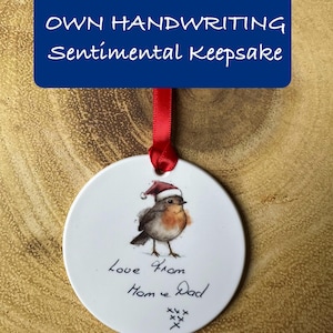 May include: White ceramic bauble featuring a robin wearing a Santa hat. The bauble has the handwritten message "love from Mom & Dad" with a few Xs.