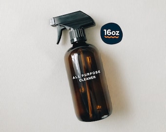May include: A brown glass spray bottle with a black trigger sprayer. The bottle has a white label that says "ALL PURPOSE CLEANER". The bottle is sitting on a white surface. The bottle is 16 ounces.