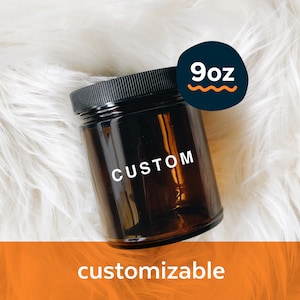 May include: A 9oz amber glass jar with a black lid. The jar is labeled "CUSTOM" and is sitting on a white fluffy surface. The jar is customizable.