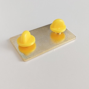 Pode incluir: Um alfinete retangular dourado com dois suportes de alfinete amarelo brilhante. O alfinete tem um design simples e minimalista, adequado para jaquetas, bolsas ou outros acess&oacute;rios. A superf&iacute;cie do alfinete &eacute; lisa e reflexiva.