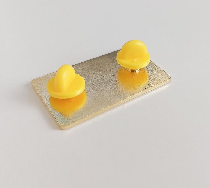 Pode incluir: Um alfinete retangular dourado com dois suportes de alfinete amarelo brilhante. O alfinete tem um design simples e minimalista, adequado para jaquetas, bolsas ou outros acess&oacute;rios. A superf&iacute;cie do alfinete &eacute; lisa e reflexiva.