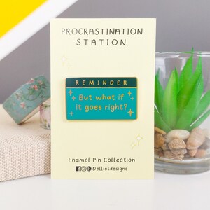 Pode incluir: Um alfinete de esmalte turquesa com o texto "But what if it goes right?" e a palavra "REMINDER" no topo. O alfinete est&aacute; em um cart&atilde;o creme com as palavras "PROCRASTINATION STATION" no topo. O cart&atilde;o tamb&eacute;m inclui o texto "Enamel Pin Collection".