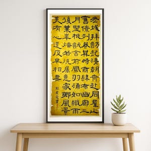 May include: A framed artwork featuring vertical Chinese calligraphy on a textured, yellowed paper background. The black ink characters are densely arranged, with a few red ink characters. The artwork is displayed on a wooden table.