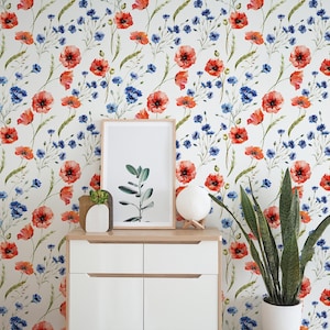 May include: A white cabinet with a framed botanical print, a decorative vase, and a modern lamp. The background features a floral wallpaper with red poppies and blue cornflowers.