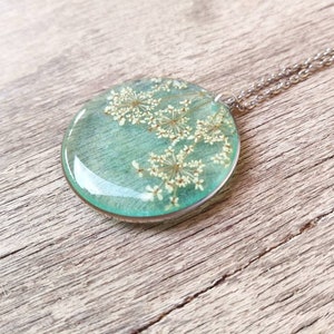 Aqua green resin pendant with inserted wild carrot flowers, thin stainless steel circle. Diameter 3 cm, thickness 5 mm.