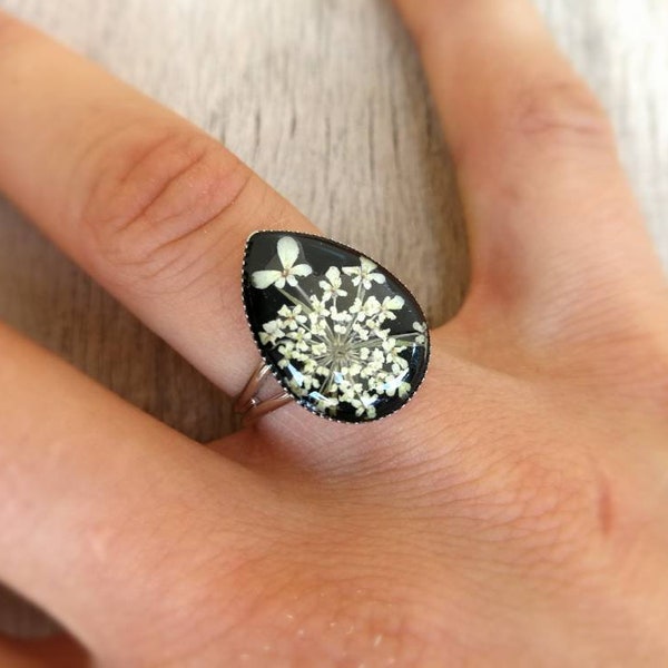 Bague femme réglable en métal argenté. Cabochon goutte en résine noire avec véritable fleur insérée, 1,4 x1,8 cm.