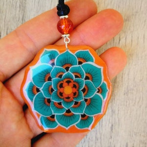 Necklace with large flower-shaped pendant in handcrafted resin. Orange and emerald green floral pattern. Width 50mm.