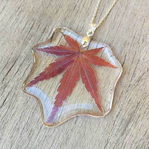 Blattförmiger Anhänger aus transparentem Harz mit eingelegtem Ahornblatt. H5,3xL5,5 cm. Kettenlänge und Farbe nach Wahl.