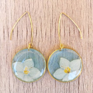 Earrings in teal resin with jasmine flowers, in gold-colored stainless steel circle, long monachella in stainless steel. H6,3xL3cm.