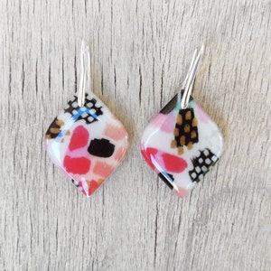 Diamond-shaped resin earrings with a white, pink, and black brushstroke motif. Silver-tone leverback closure. L 2.2 cm x H 5 cm.