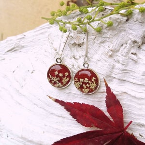 Puede incluir: Un par de pendientes de aro de plata con colgantes redondos de resina roja. Cada colgante presenta un delicado diseño de flores prensadas.