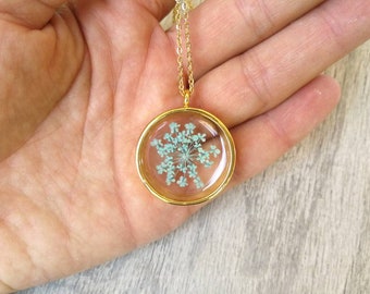 Transparent resin pendant with aqua green ammi majus flower. Ø 2.7cm, thickness 1cm. Fine stainless steel chain, gold coloured.