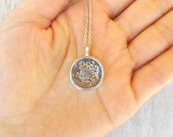 Small pendant in zinc alloy and pearl resin, with flower inserted. Diameter 1.9 cm, thickness 7 mm. Stainless steel chain.