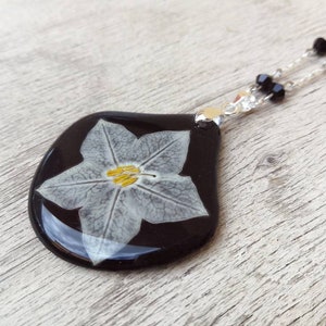 Drop pendant in black resin, with real star jasmine flower. L3.8xH4 cm. Stainless steel chain with hand-assembled crystals.